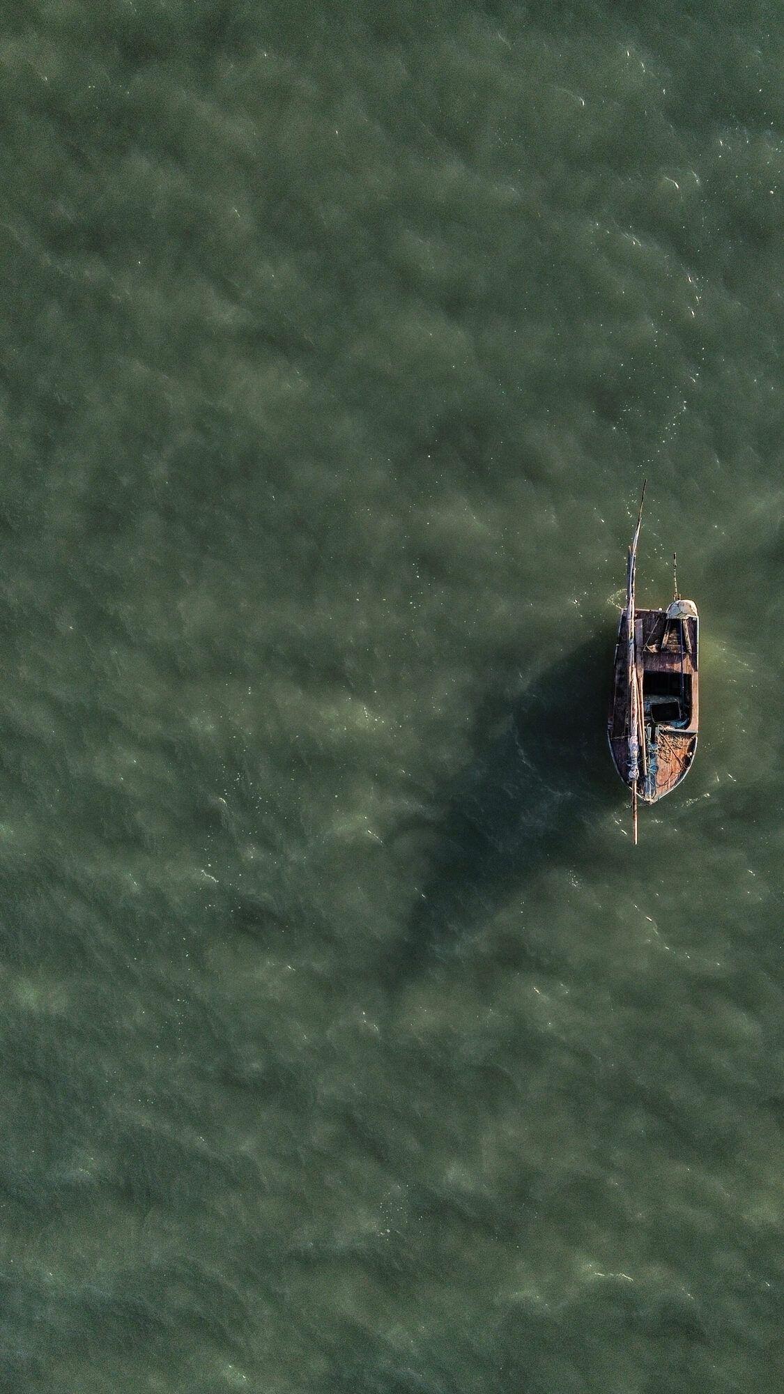Vue aérienne d'un petit bateau de pêche ancré dans une eau vert émeraude.