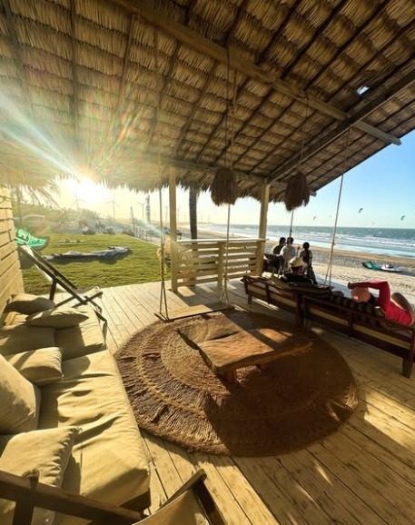 Deck coberto de palha com sofás e vista aberta para a praia e o mar.