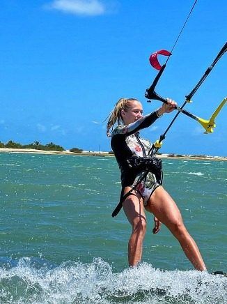 A woman kitesurfs in a shallow, green-tinted lagoon.