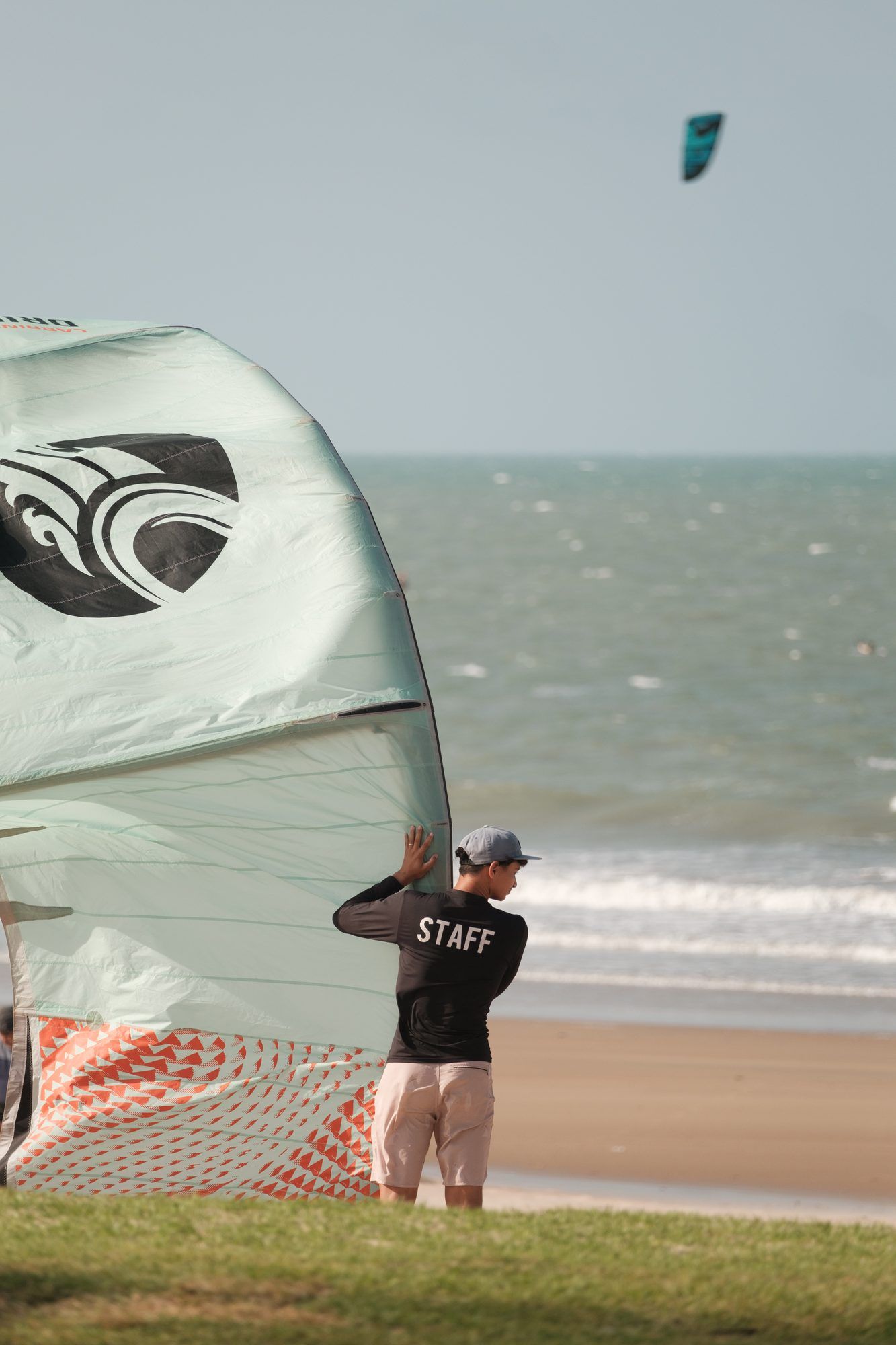Membro da equipe observa o mar segurando uma pipa, outra pipa voando ao longe.
