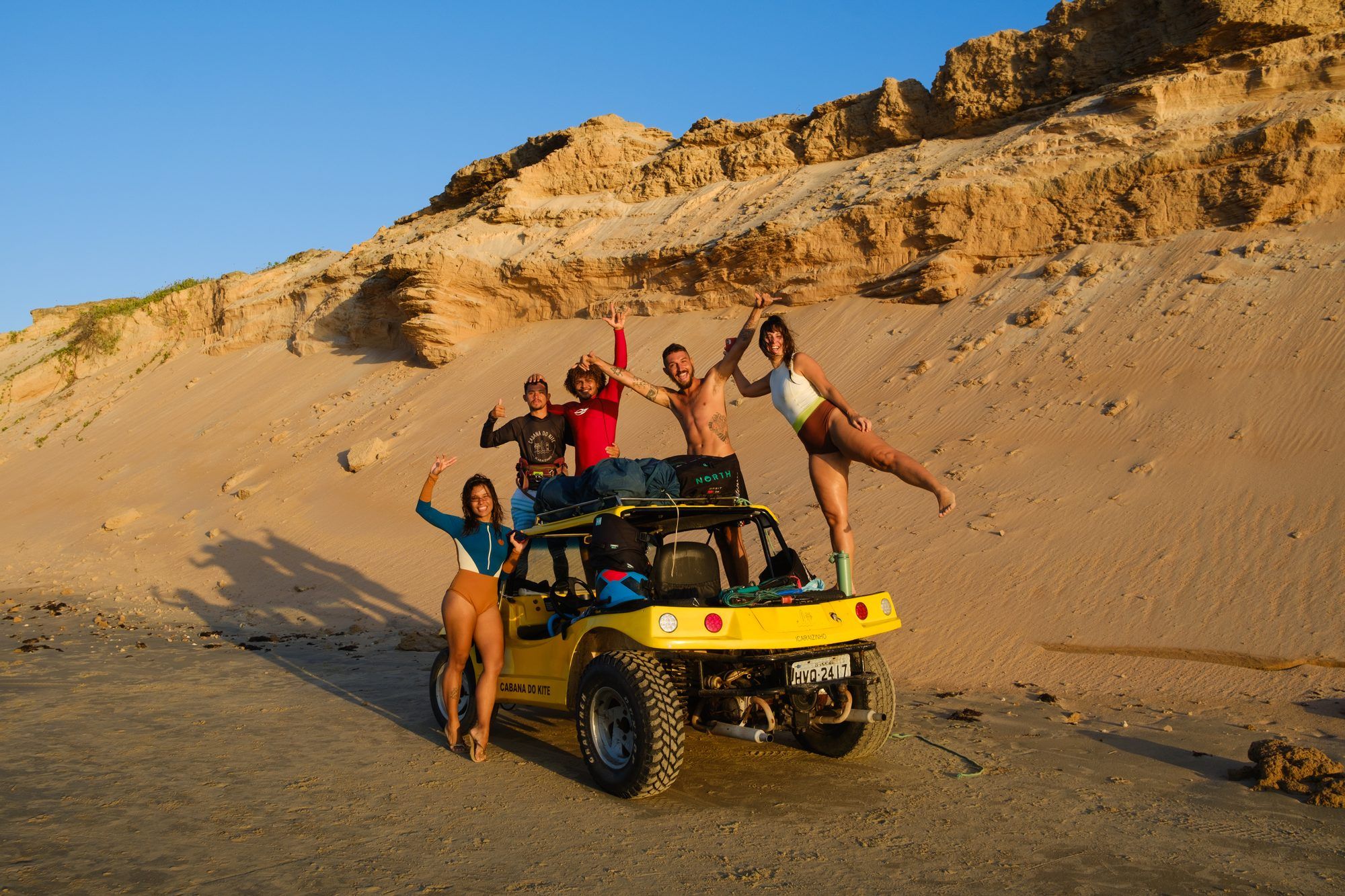A group of friends celebrate on top of a yellow beach buggy at sunset.