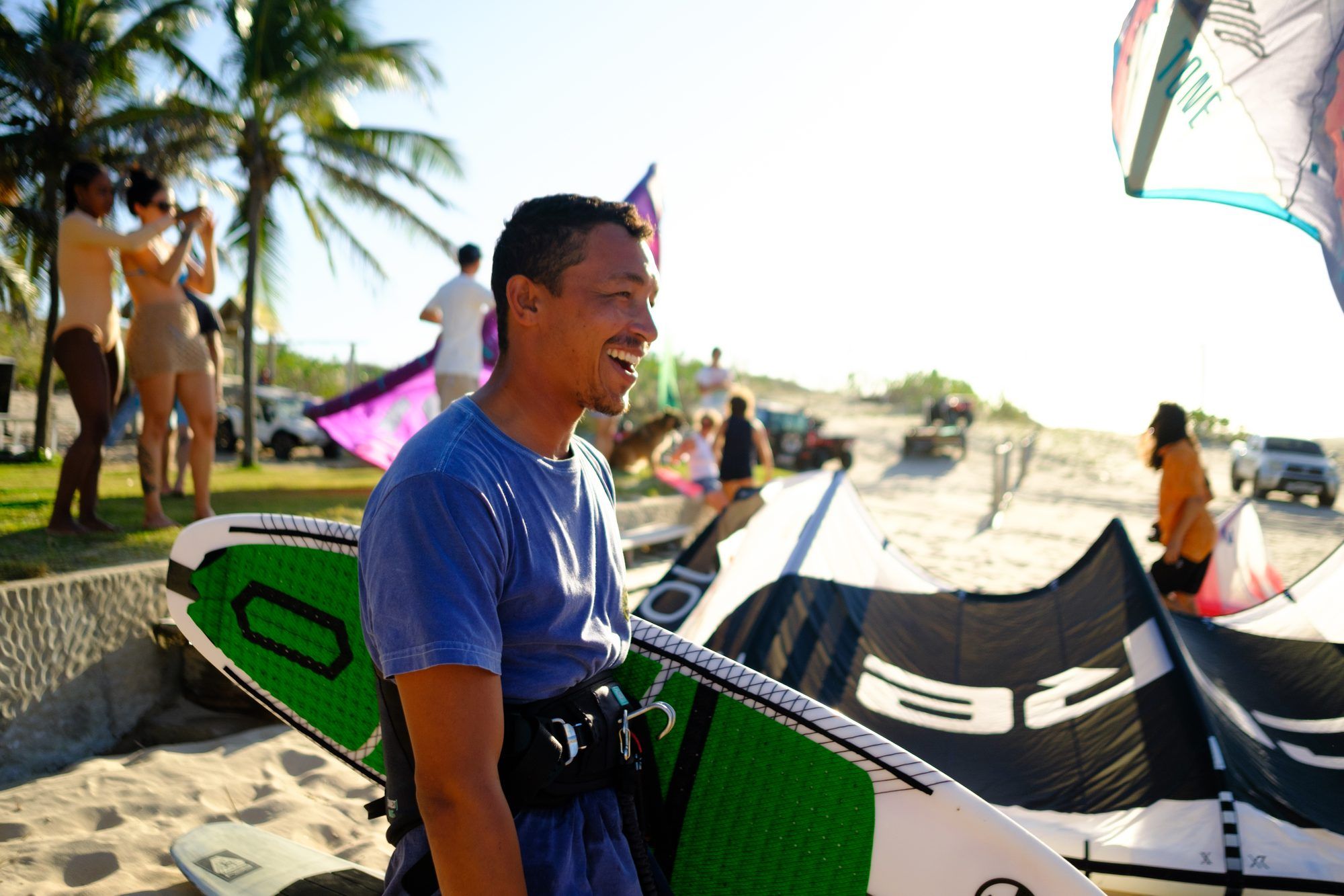 A smiling instructor carries a kite board along the beach.