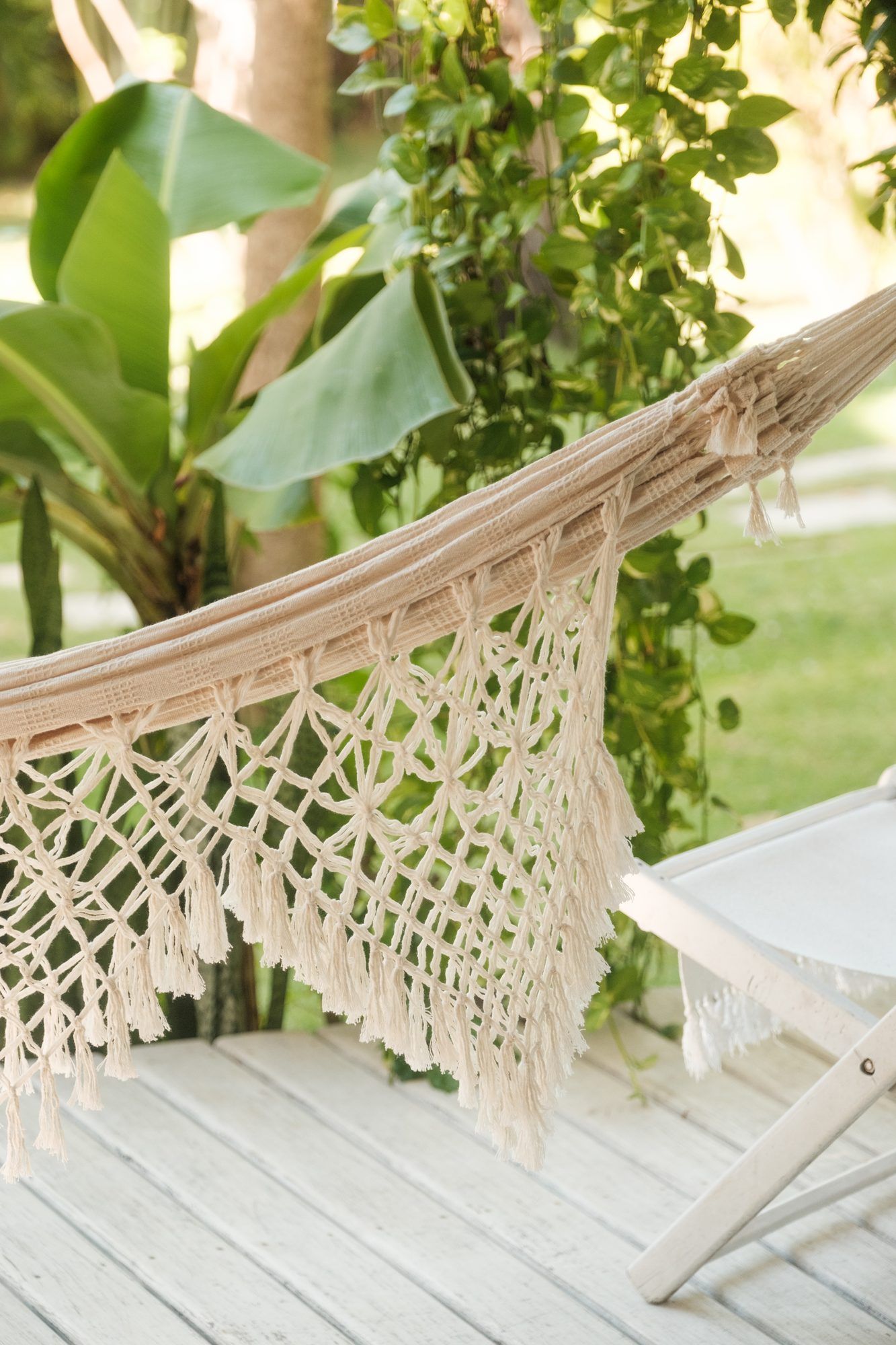 Una hamaca de macramé colgada en una galería, rodeada de plantas tropicales.