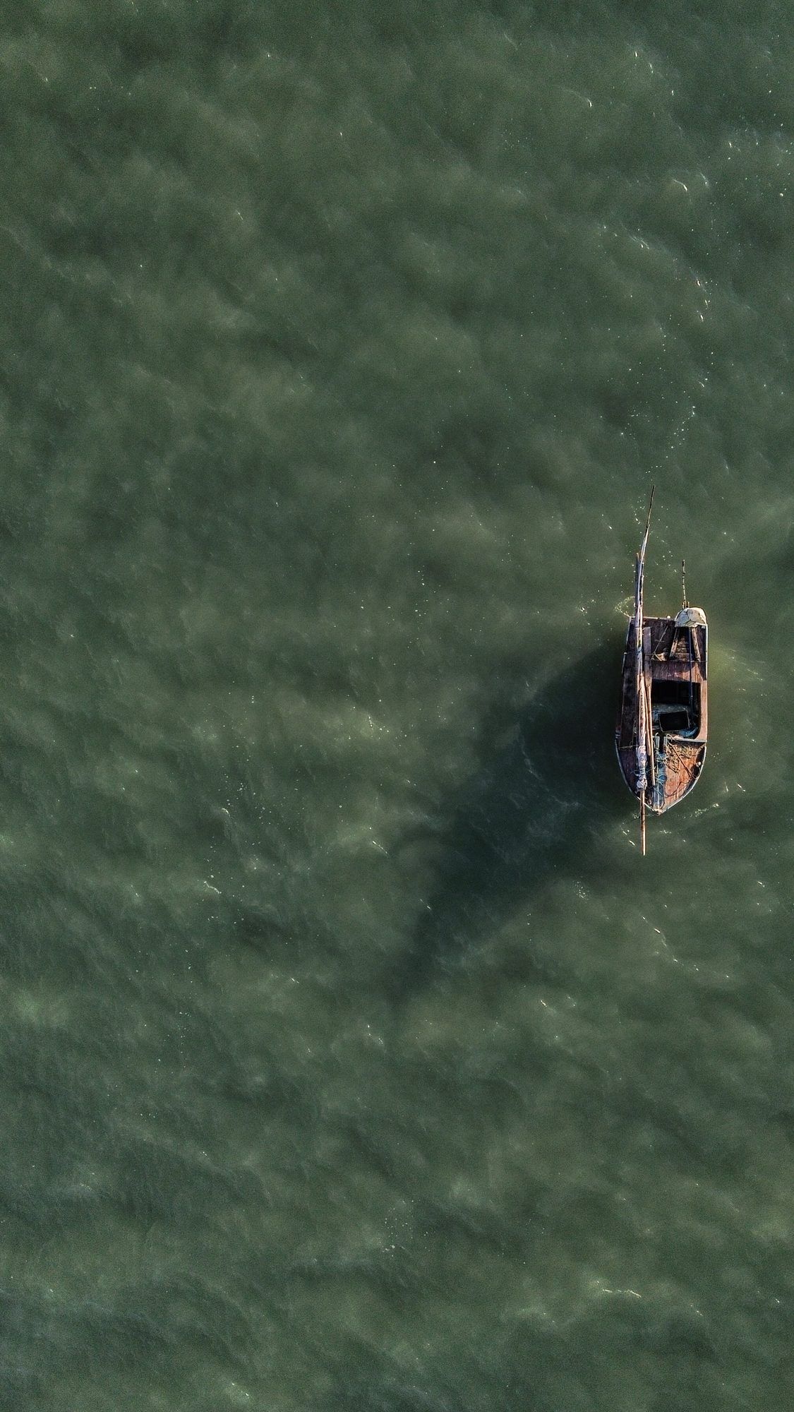 Vista aérea de um pequeno barco de pesca ancorado em água verde-esmeralda.
